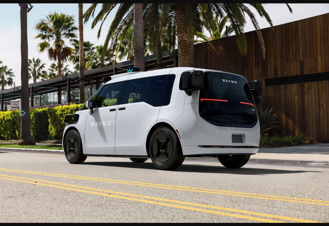 Waymo Ojai autonomous electric robotaxi driving on a palm-lined street