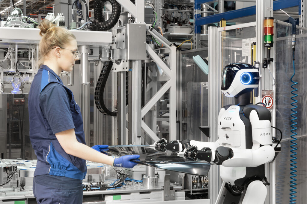 A BMW employee and Hexagon's AEON humanoid hold a metal component at BMW Group Plant Leipzig.