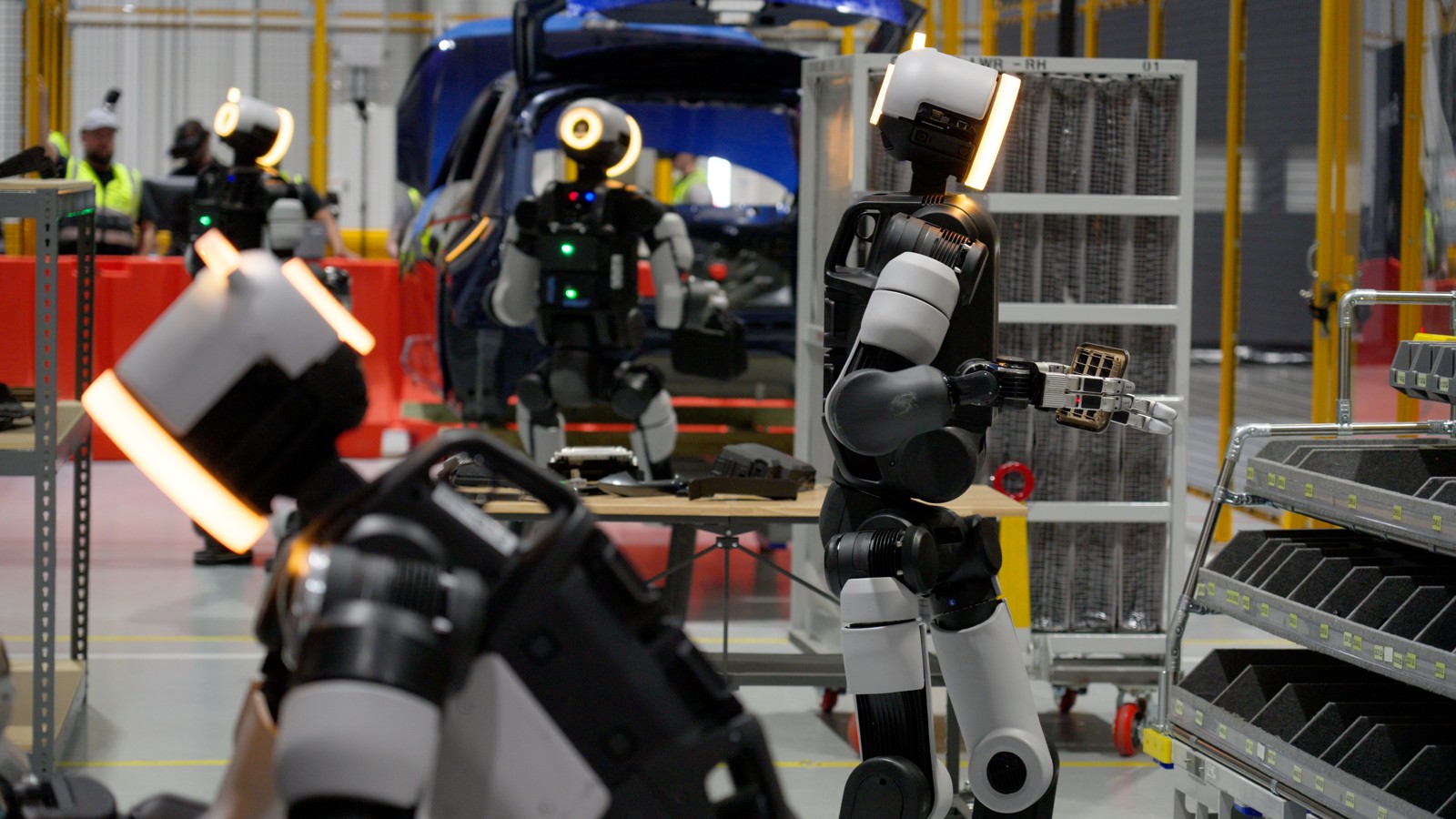 Atlas robots beside automotive parts racks in a manufacturing setting.